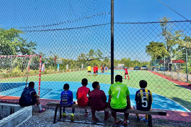 The boys watching their friends practicing football.