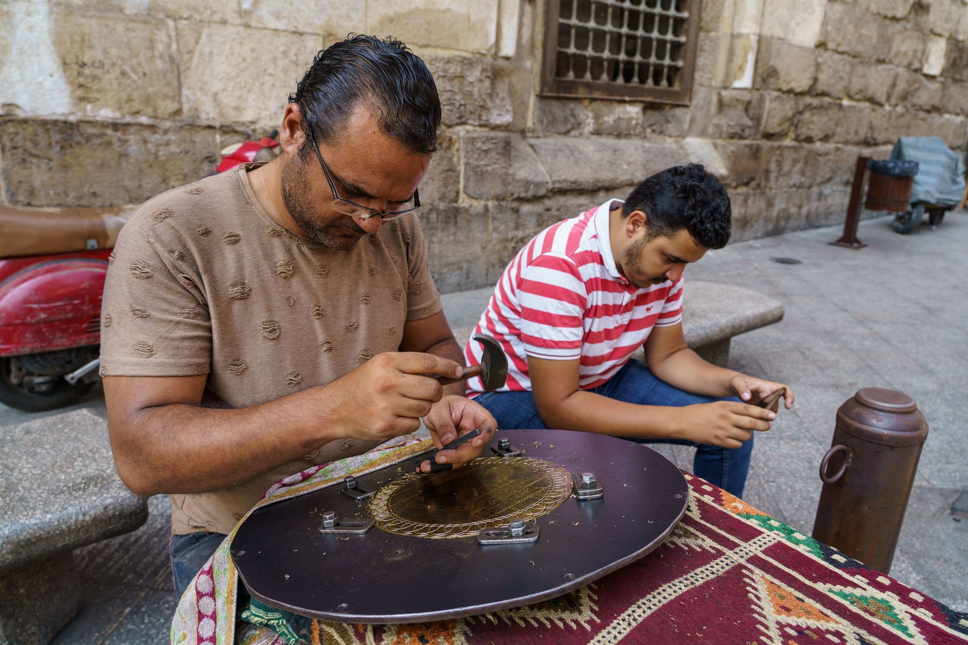 Artisan crafts ornate designs on brass to sell at his shop on the streets of North Africa.  Image by Garrett N